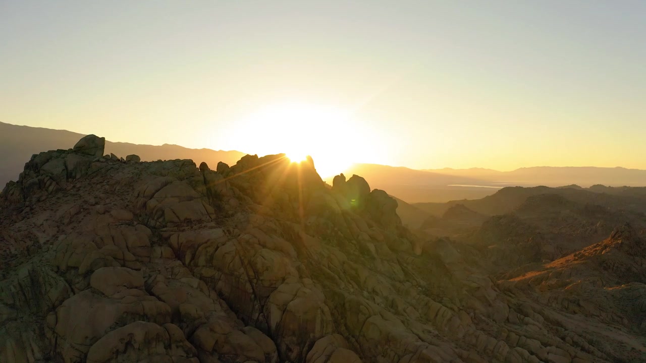 Tomada de drone revelando o nascer do sol atrás de formações rochosas escarpadas, Alabama Hills