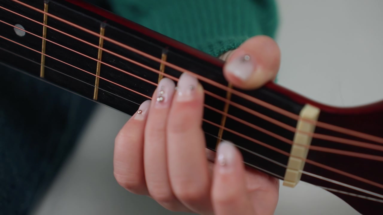 Closeup hand on acoustic guitar neck, guitarist practicing chord fingering in new apartment with green sweater sleeve, decorated nails, warm natural light, intimate home music session with moving