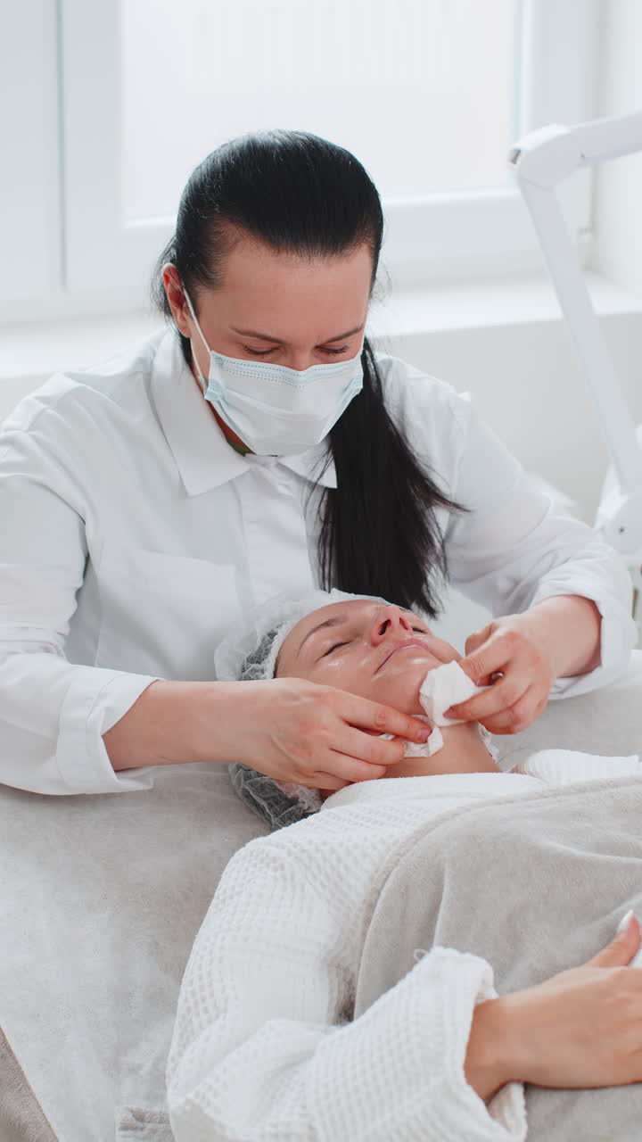 Cosmetologist doctor wipes woman face and neck cleaning procedure with cotton wipes in beauty clinic