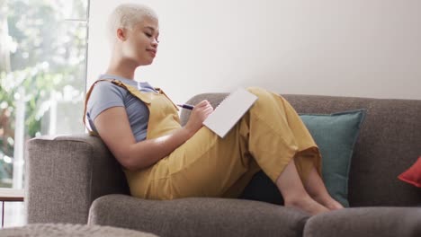 Happy-biracial-woman-taking-notes-and-sitting-on-couch-in-slow-motion