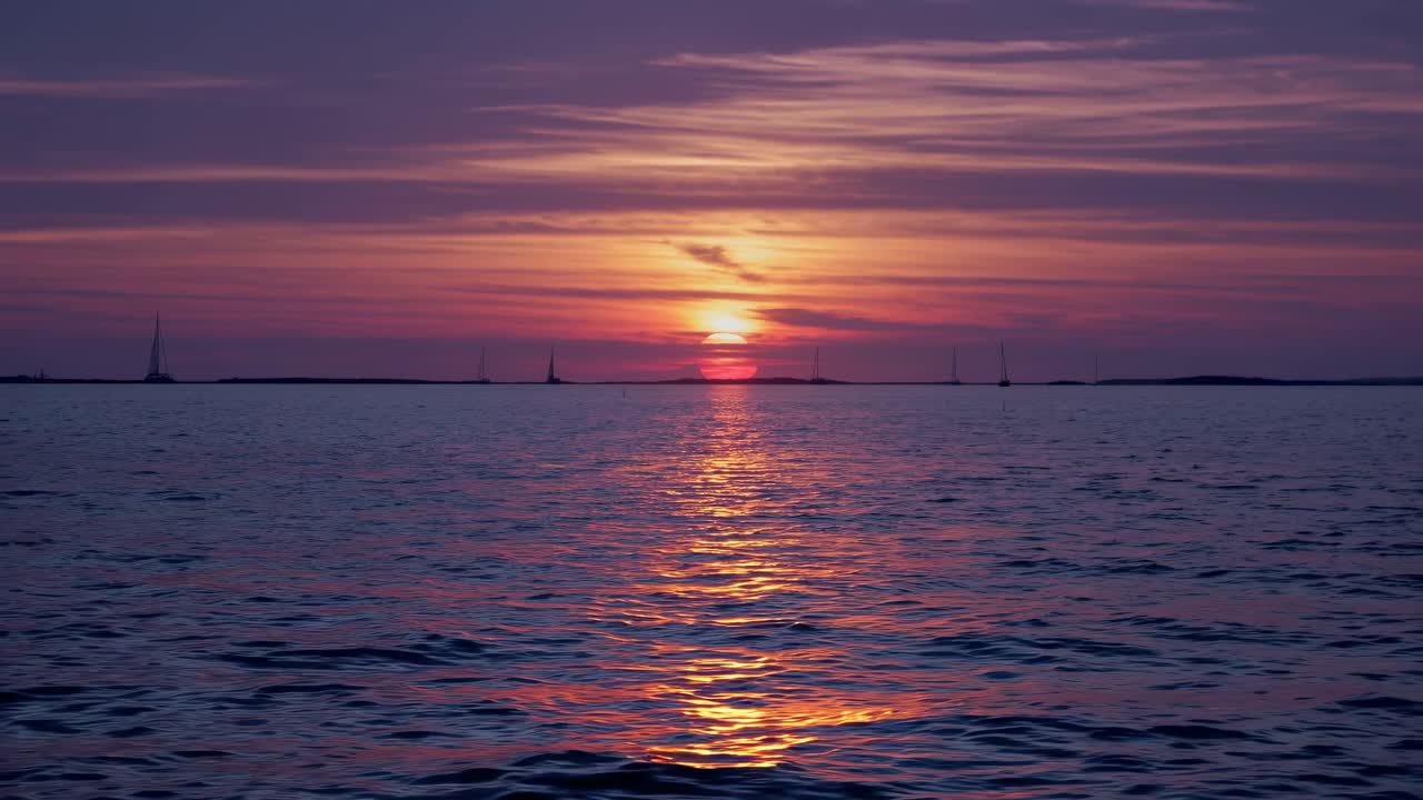 A serene sunset over the ocean, captured from a low angle. The vibrant hues reflect on the water