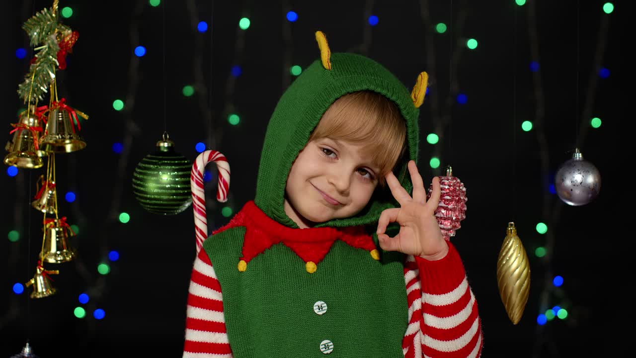 Blonďatá dospívající dívka v kostýmu vánočního skřítka ukazuje gesto OK.