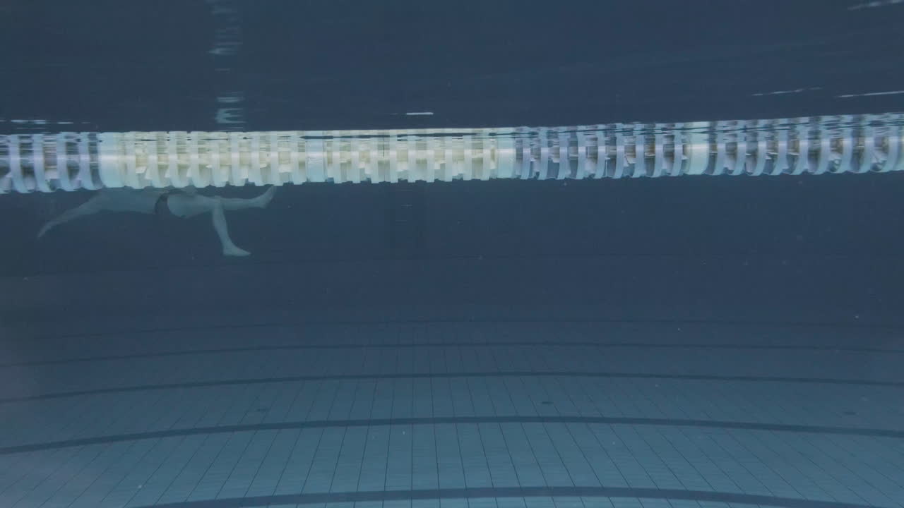 실내 수영장에서 수영 모자와 고글을 쓴 젊은 여성 수영 선수의 수중 측면 사진