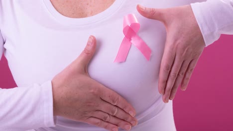 Video-of-midsection-of-caucasian-woman-wearing-pink-cancer-awareness-ribbon,-with-pink-background