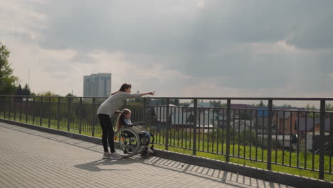 woman shows city architecture to little girl in wheelchair