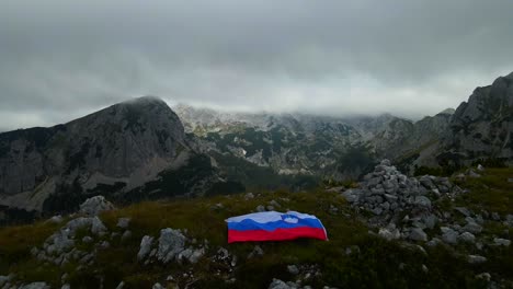 footage of a slovenian flag set on top of mountains in the alps filmed with a drone in 4k with forwarding movement with cloudy weather and mist all over the place