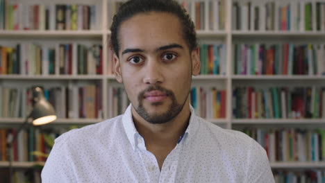 portrait-of-attractive-young-hispanic-man-student-thinking-pensive-turns-head-looking-serious-at-camera-in-study-library-background