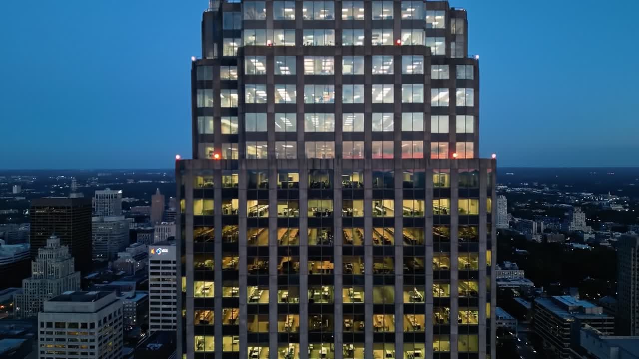 Aerial View of Majestic Urban Skyscraper at Dusk with Illuminated Windows and Vibrant Cityscape in the Background Showcasing Modern Architecture