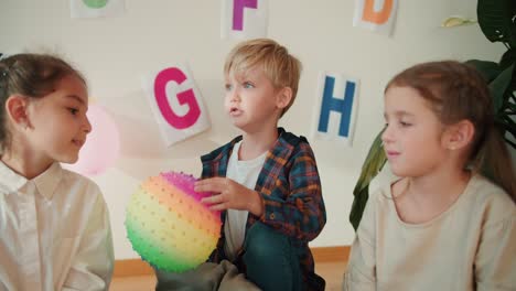 Little-preschool-children-pass-each-other-a-colorful-ball-and-talk-about-themselves-during-their-first-lesson-in-a-school-preparation-club.-Young-children-learn-to-communicate-with-each-other-using-a-ball-and-have-a-little-therapy-before-a-school-readiness-club-activity