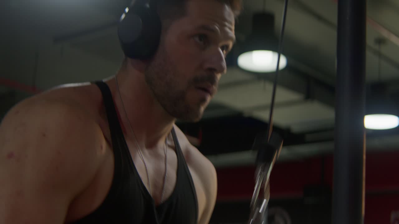 Um homem treinando bíceps na academia com corda, com luz pontual por trás, em close-up.