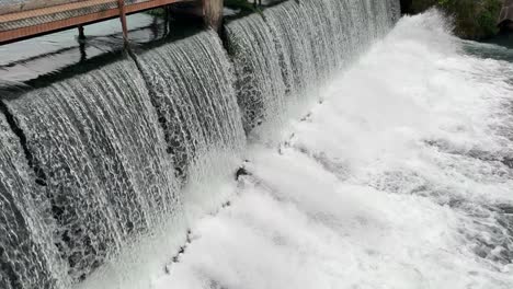 water flowing through a dam into a spring below 4k 30fps drone angle