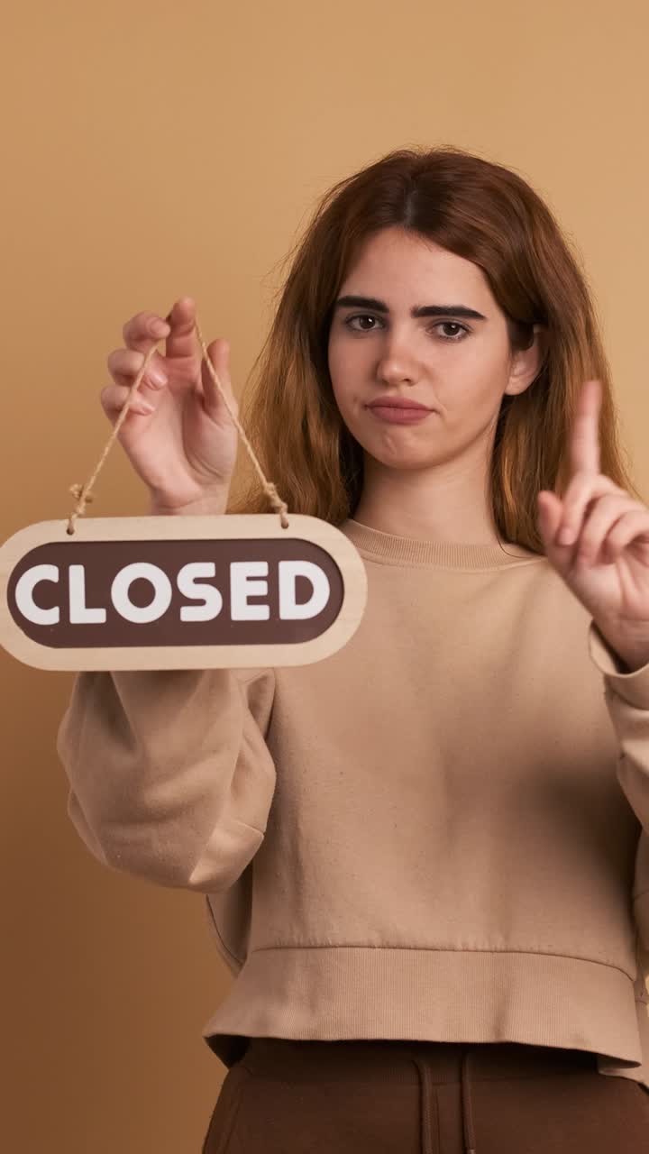 Young woman standing with closed sign near wall. Vertical Footage