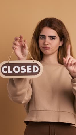 young woman standing with closed sign near wall. vertical footage