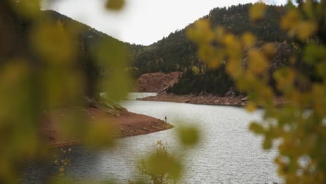 Establishing-shot-of-fisherman-on-reservoir,-through-autumn-leaves