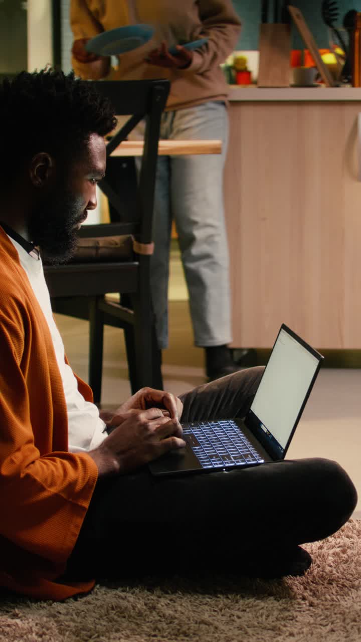 Vertical Video African american person, relaxing with laptop, sitting on the floor at home