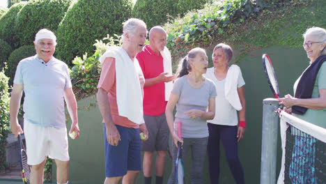 diverse group of happy male and female seniors talking at sunny outdoor tennis court, slow motion