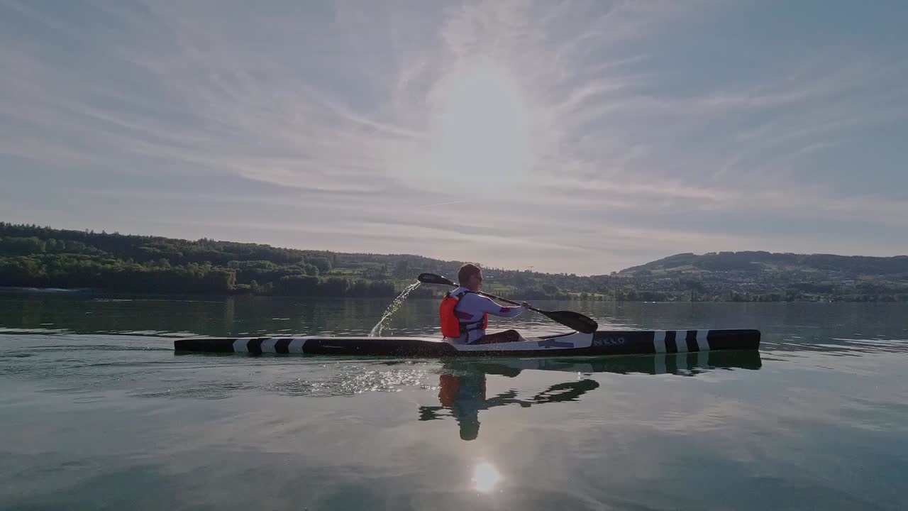 hombre en kayak en un lago tranquilo en suiza durante la puesta de sol