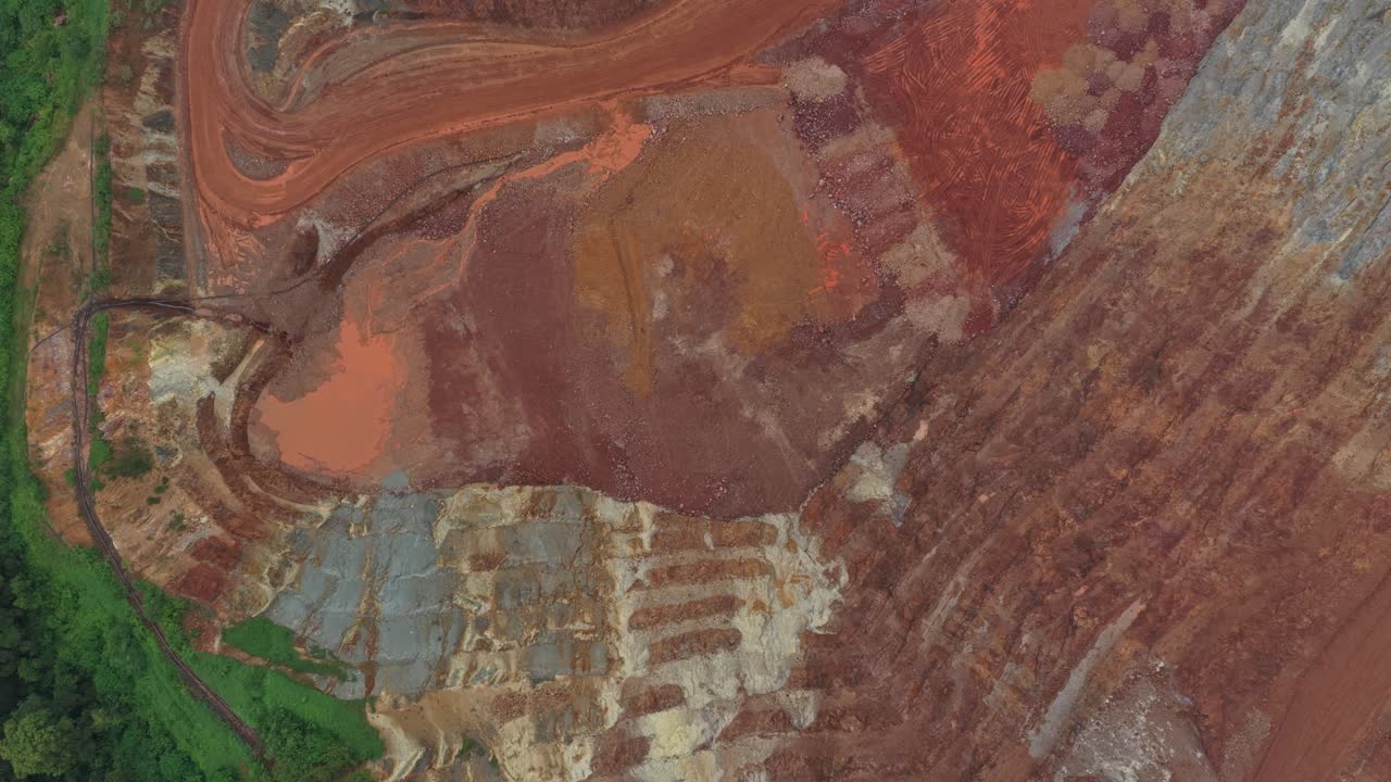 Drone's perspective flying over an open cast bauxite mine. The vast industrial quarry shows different layers of mineral soil and earth