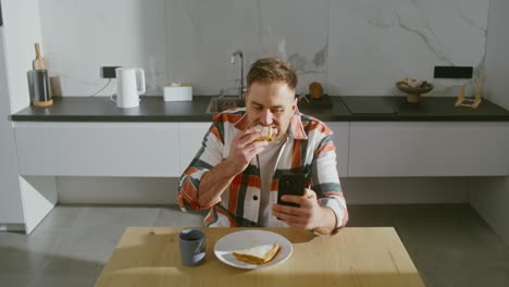 man eating breakfast and using his phone in the kitchen