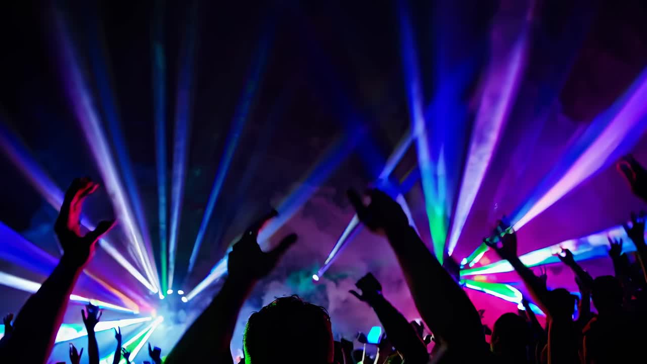 Vibrant concert scene with colorful lights and raised hands, captured from a low-angle
