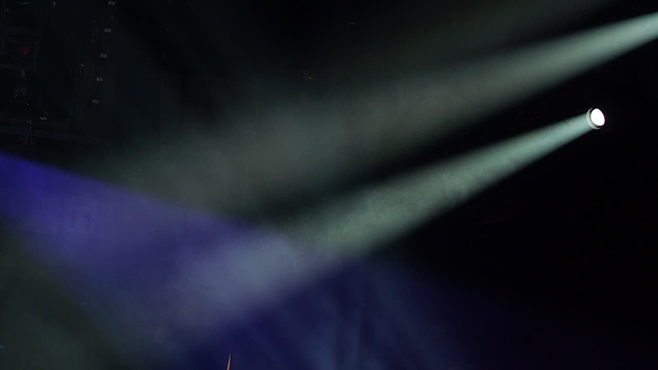 Dramatic white light beams in the smoke created by the spotlights during showtime in a concert hall in the darkness, with copy space