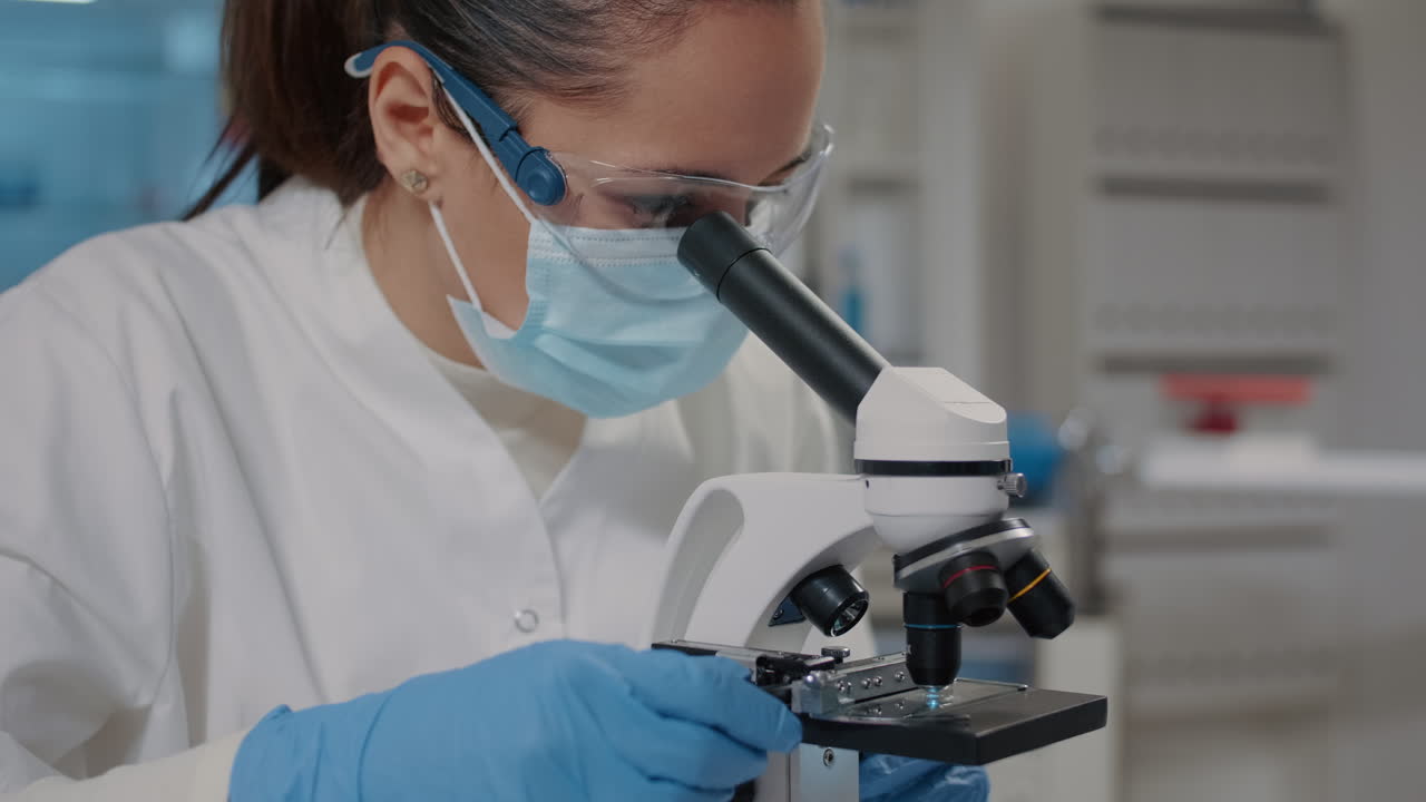 Biologist with face mask using microscope in science laboratory