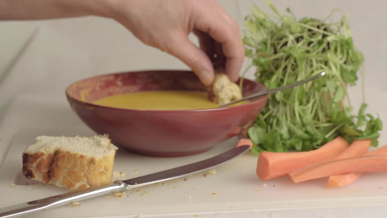 Hand dipping bread into fresh carrot and coriander soup wide shot