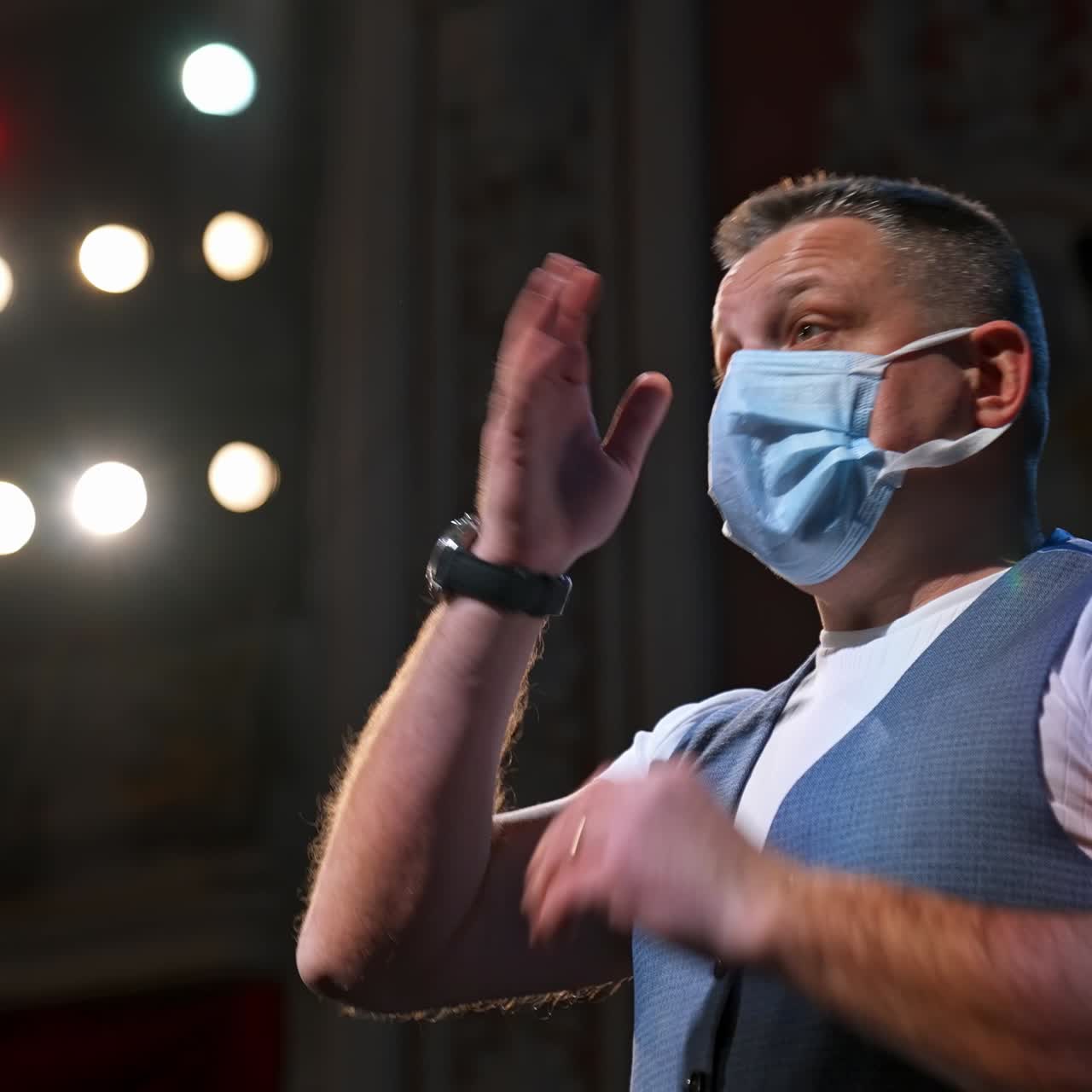 Uomo sul palco del teatro. Uomo di mezza età che indossa una mascherina medica durante il coronavirus sotto i riflettori. Vista laterale.