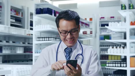 primer plano de un médico asiático con un estetoscopio usando un teléfono inteligente mientras está de pie en la farmacia
