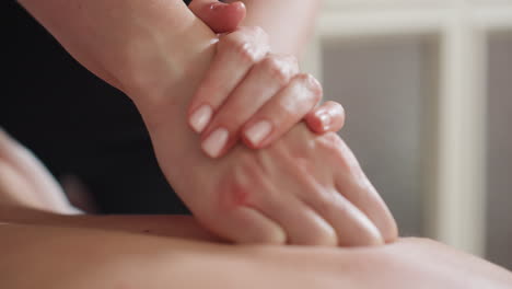 closeup view of female massage therapist pressing down on client back using folded hands technique for deep pressure massage, showing gentle care and relaxation in soft, well-lit indoor setting