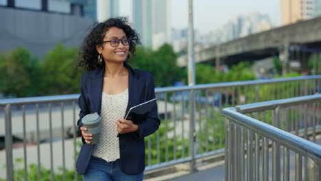 woman walking in city with coffee and laptop