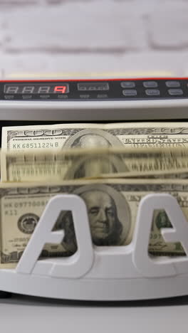 electronic cash counting machine. bank financial operations and calculating dollar banknotes. female hand puts paper money into automatic equipment for counting bills. vertical video