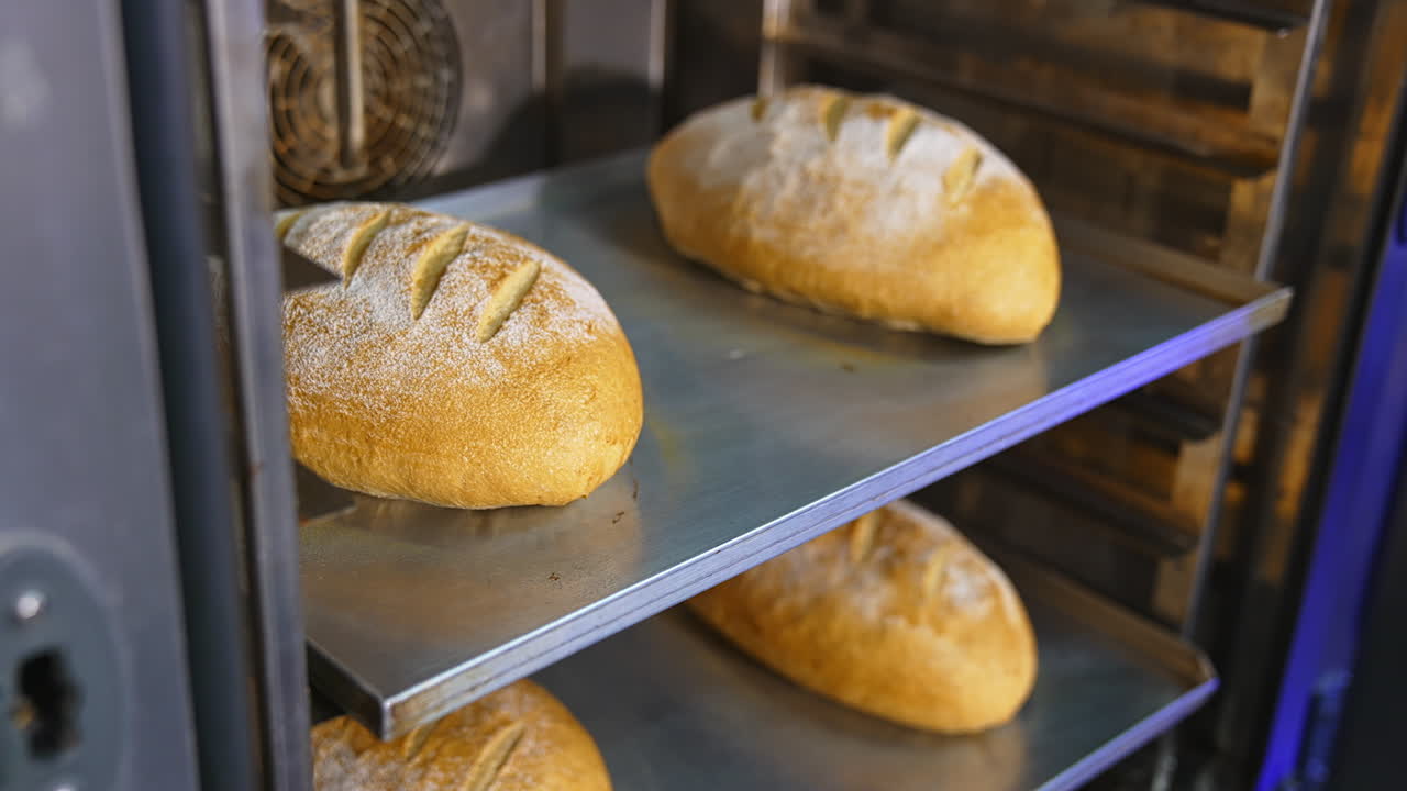 Baker's hands pull freshly-baked loaves from the oven. Making tasty brown bread at bakery. Close up.