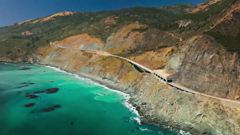 idyllic scenery of turquoise ocean and crushing waves at the rocks. highway passing through the mountains. sunny day backdrop.