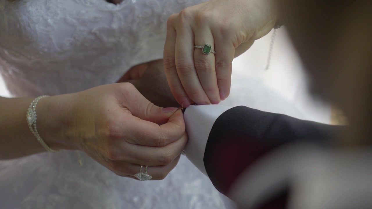 Primo piano della sposa che sistema il gemello dello sposo durante la preparazione del matrimonio.