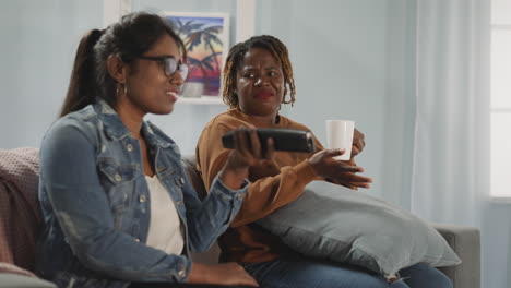 woman looks for interesting channel while friend drinks tea