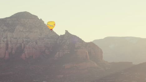 Yellow-hot-air-balloon-rises-near-Capitol-Butte-in-Sedona-on-crisp-morning