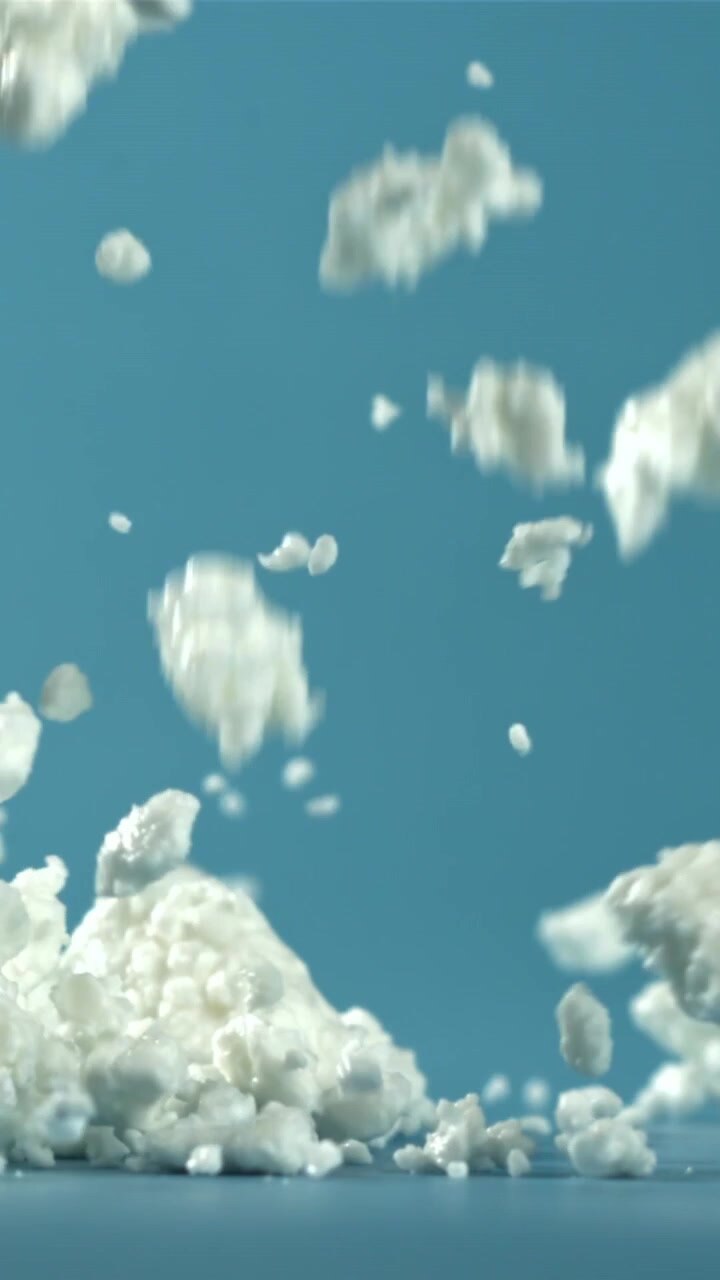 Particelle bianche friabili che cadono al rallentatore su superficie blu