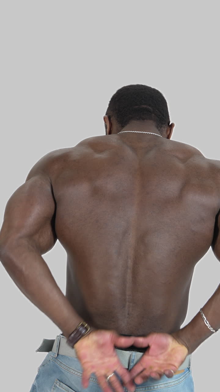 Back muscles of a black athlete. Shirtless african american sportsman shows his trained body isolated on white. Rear view. Vertical video