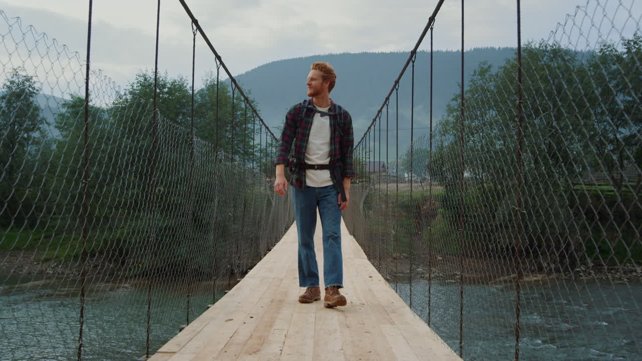 Viaggiatore sorridente saluta con la mano sul ponte del fiume. Escursionista si gode la vacanza in montagna.