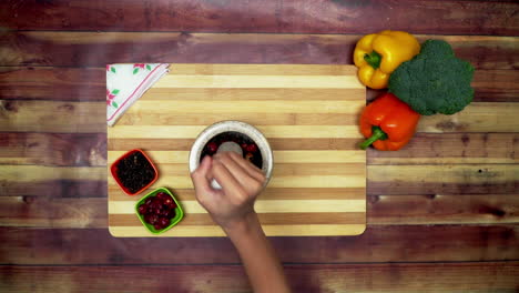 A-Top-view-of-grinding-the-red-chili-and-black-pepper-in-the-pestle-by-band,-two-big-yellow-and-red-capsicums-and-a-green-broccoli-on-the-table