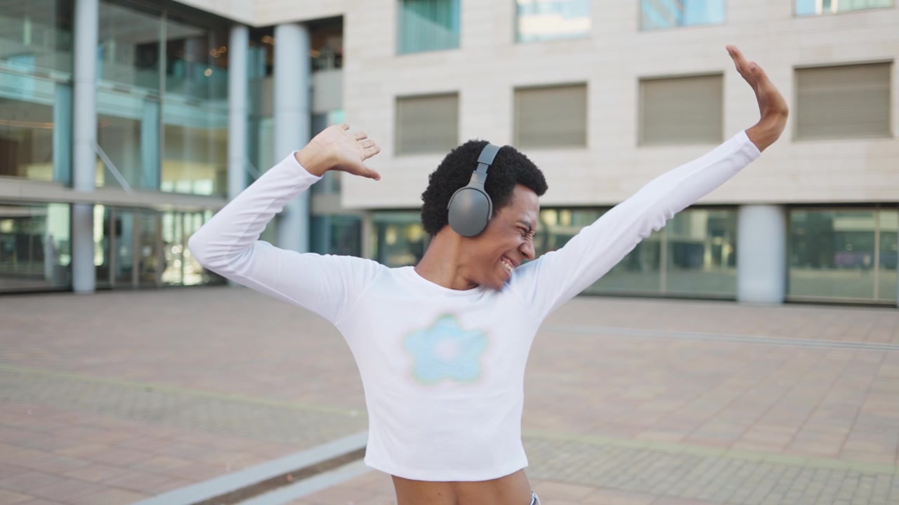 Joyful Young Black Man Dancing to Music with Headphones in City