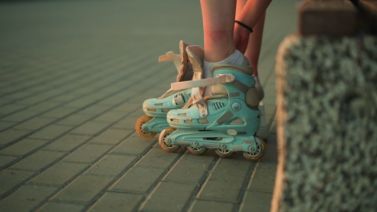 Side view of young lady removing strap of left roller skate while sitting on pavement, with two white sneakers placed next to her, evening lighting creates a calm atmosphere