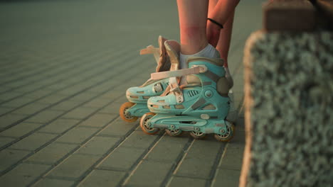 side view of young lady removing strap of left roller skate while sitting on pavement, with two white sneakers placed next to her, evening lighting creates a calm atmosphere