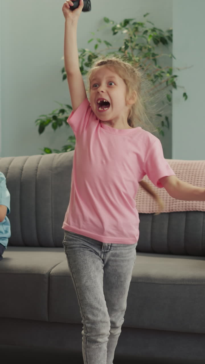 Toothless blonde girl jumps feeling proud and happy to win video game playing with little brother. Happy preschooler and sad boy in living room