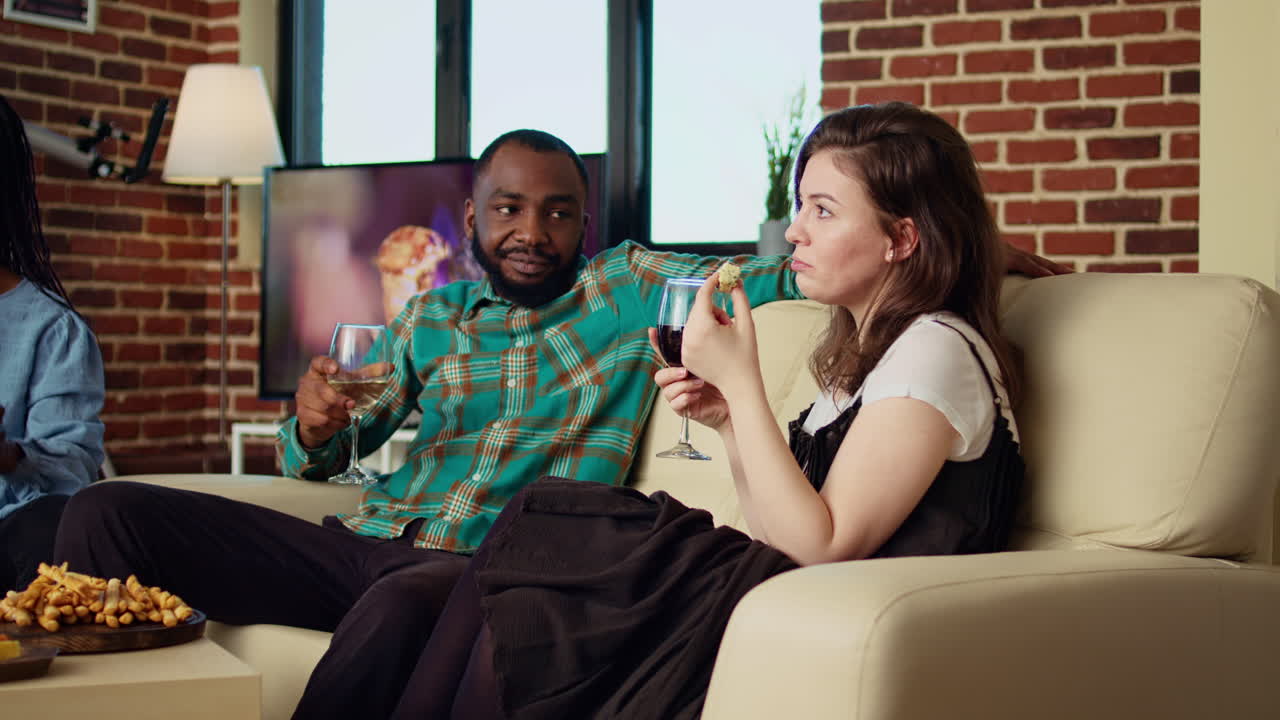 Man at social gathering flirting with woman on couch while enjoying glass of wine