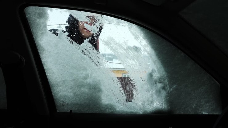 Snow Covering Car Window Being Cleared By A Woman In Winter