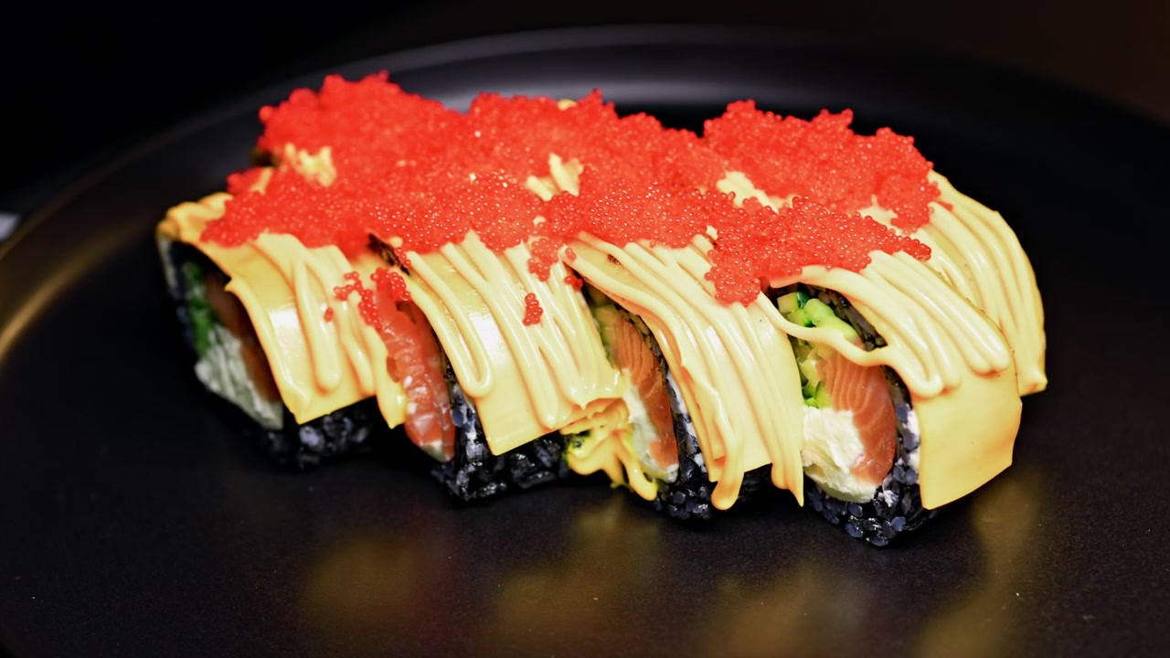 Sushi-Rolle mit Lachs, schwarzem Reis und roten Belägen, serviert auf einem schwarzen Teller in einem Restaurant.