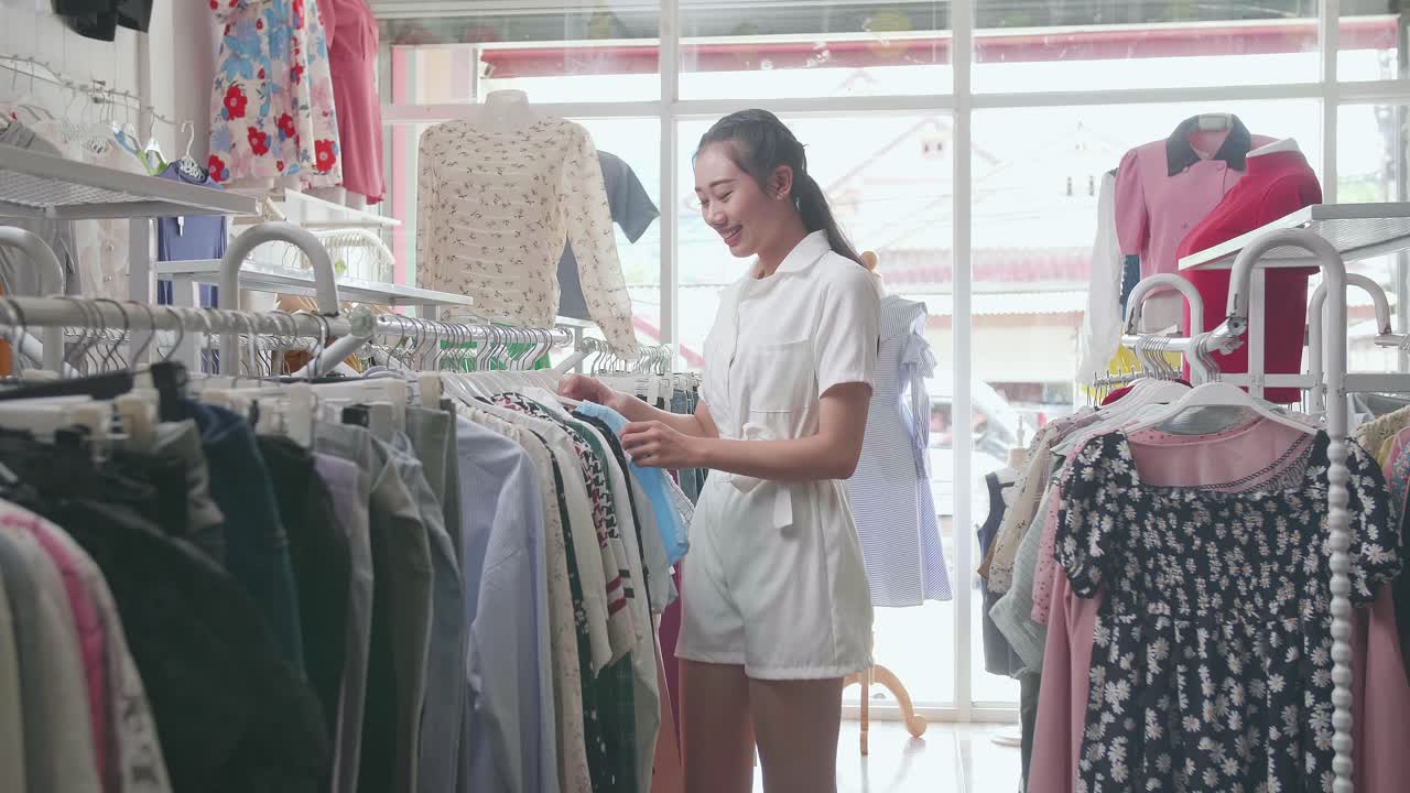 젊은 아시아 여성 은 부티크 에서 쇼핑 하는 동안 거 에 있는 옷 을 선택 하는 것 을 즐긴다