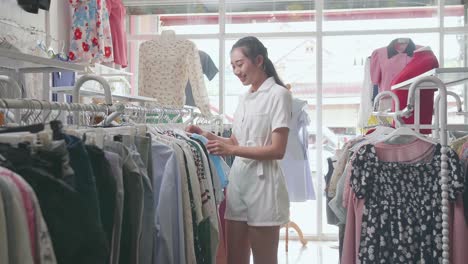 young asian woman enjoys choosing clothing items on hangers while shopping at the boutique